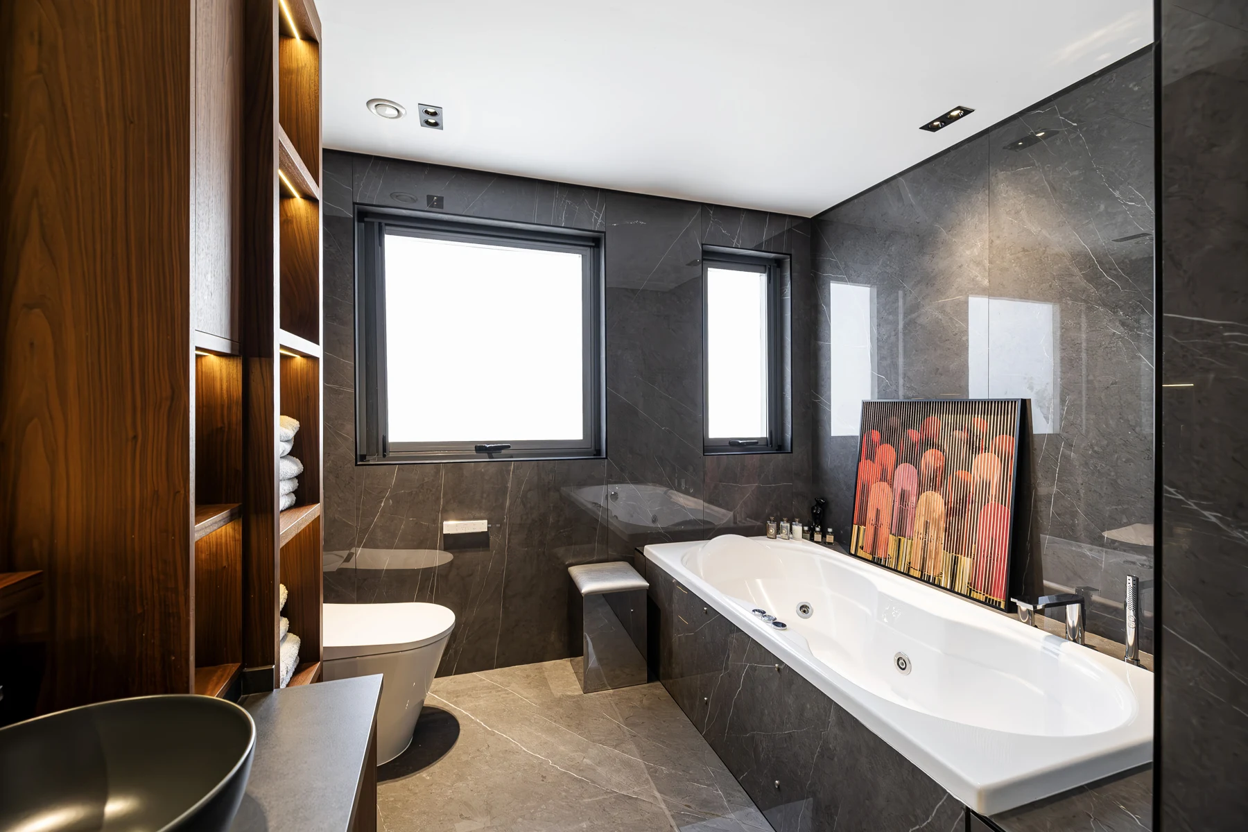 Sidra 1 Villa — Illuminated timber niches introduce warm task lighting within the stone-lined bathroom.